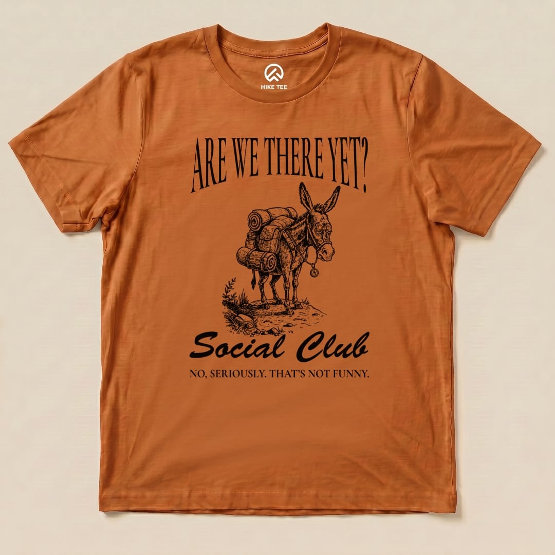 Brown graphic t-shirt featuring the slogan "ARE WE THERE YET? Social Club" with a humorous illustration of a donkey carrying hiking gear.