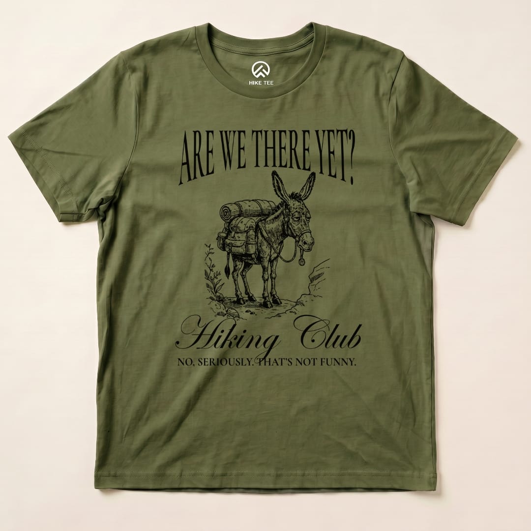 Olive green graphic t-shirt featuring a donkey with a backpack, labeled "Are We There Yet? Hiking Club" with the slogan below.