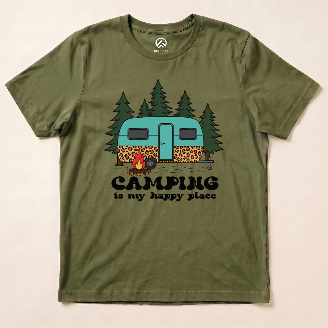 The "Camping is My Happy Place Shirt" features a vintage camper surrounded by trees and a campfire in a playful design.