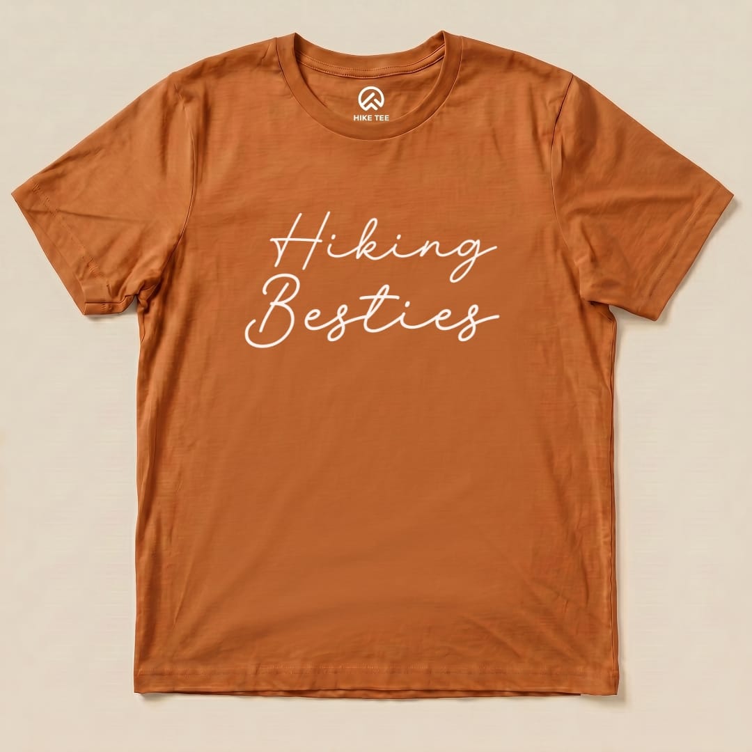 Graphic t-shirt in earthy orange featuring the phrase "Hiking Besties" in a playful, cursive font.