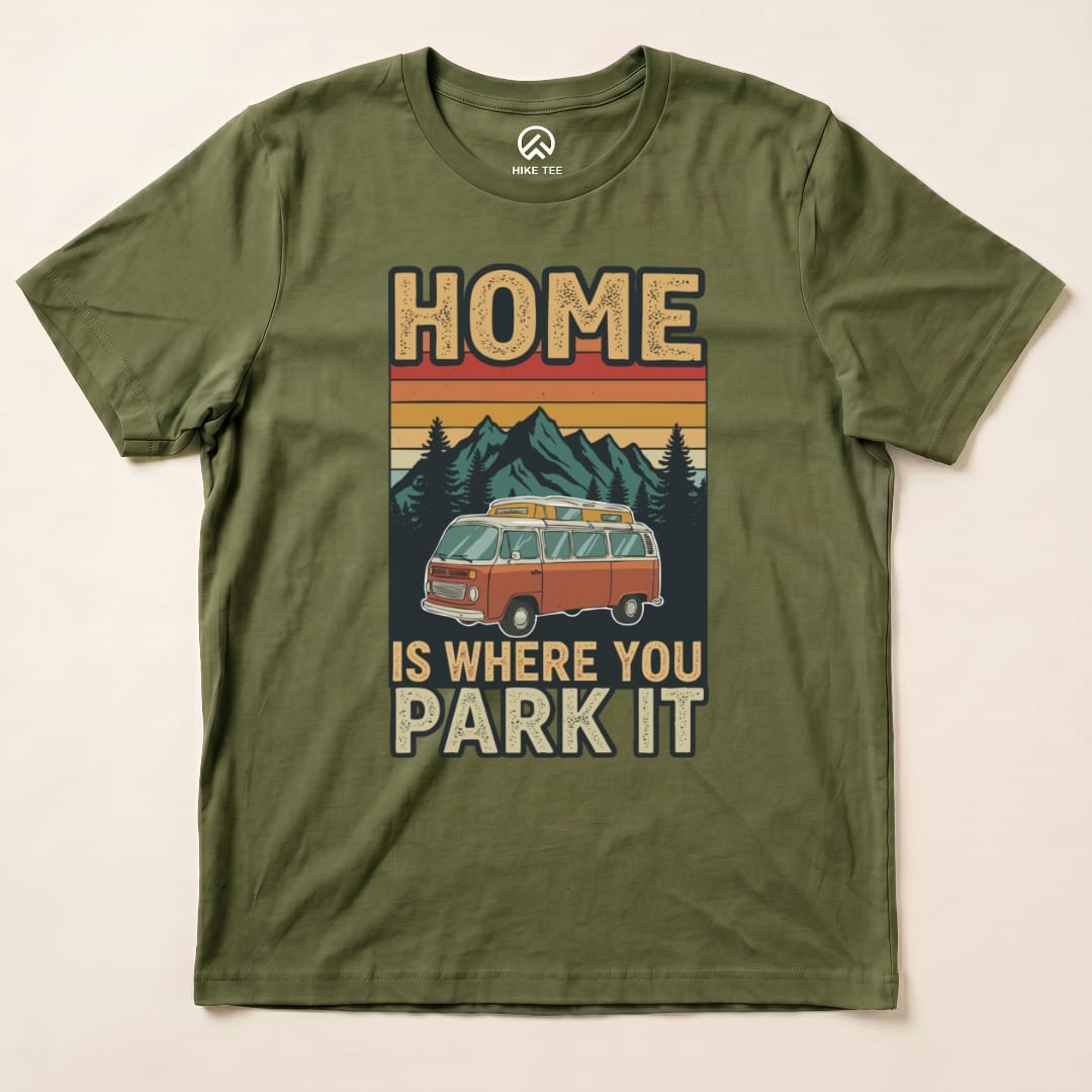 Graphic t-shirt featuring the design "HOME IS WHERE YOU PARK IT" with a vintage van, mountains, and trees in earthy tones.