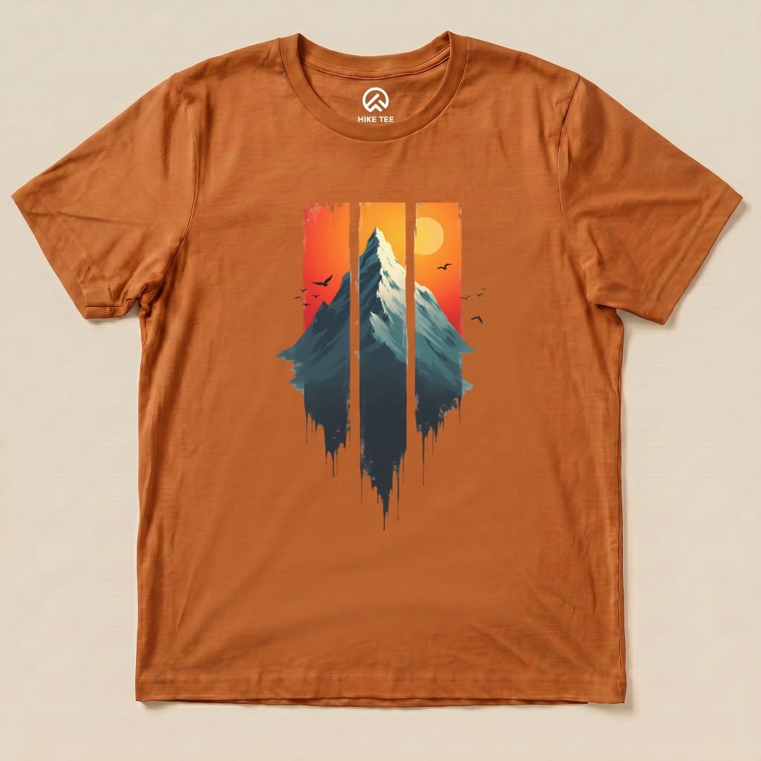 The Mountain Sunset Shirt features a colorful graphic of a mountain scene with a sunset and birds, printed on a rust-colored t-shirt.