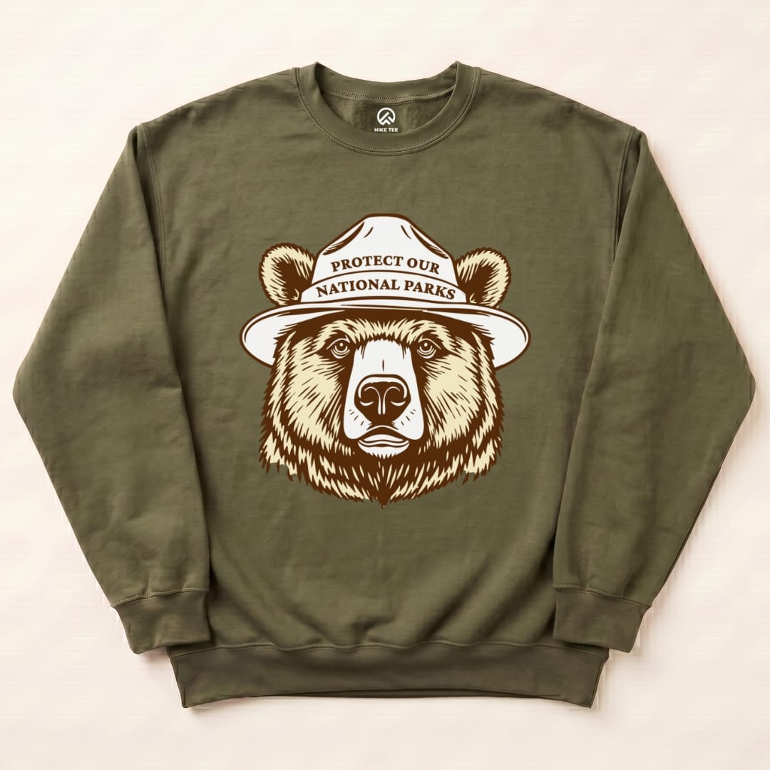 Olive green "Protect Our NP Sweatshirt" featuring a graphic of a bear wearing a park ranger hat with the slogan printed above.