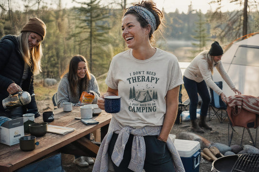 Woman laughing at a cozy forest campground while wearing a funny camping T-shirt with friends and camping gear nearby.