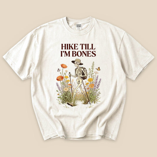 Ivory Hike Till I'm Bones T-Shirt with a skeleton hiker among wildflowers graphic