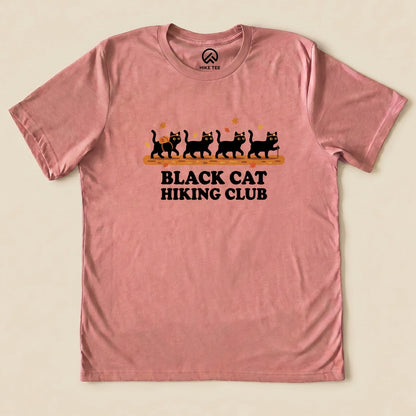 Heather Mauve Black Cat Hiking Club Shirt with a row of black cats walking on a log with autumn leaves graphic