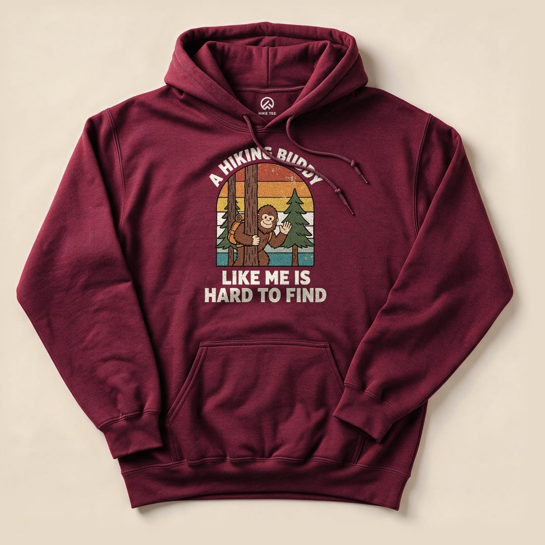 A maroon hoodie featuring a whimsical graphic of a monkey peeking from behind a tree with the text "A Hiking Buddy Like Me Is Hard To Find.