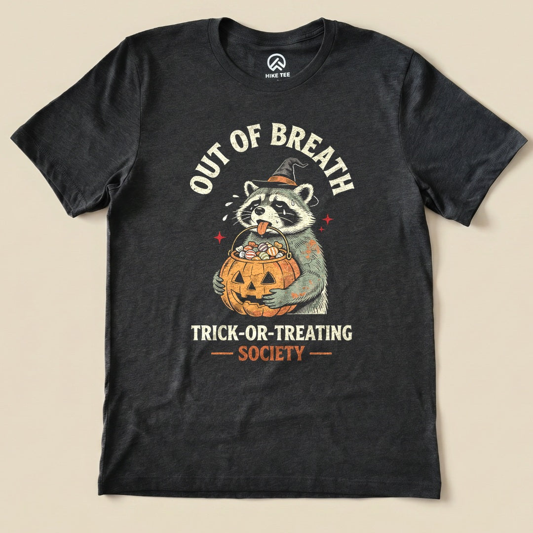 Dark Grey Heather Out of Breath Trick-or-Treating Society Shirt with a raccoon witch holding a pumpkin full of candy graphic
