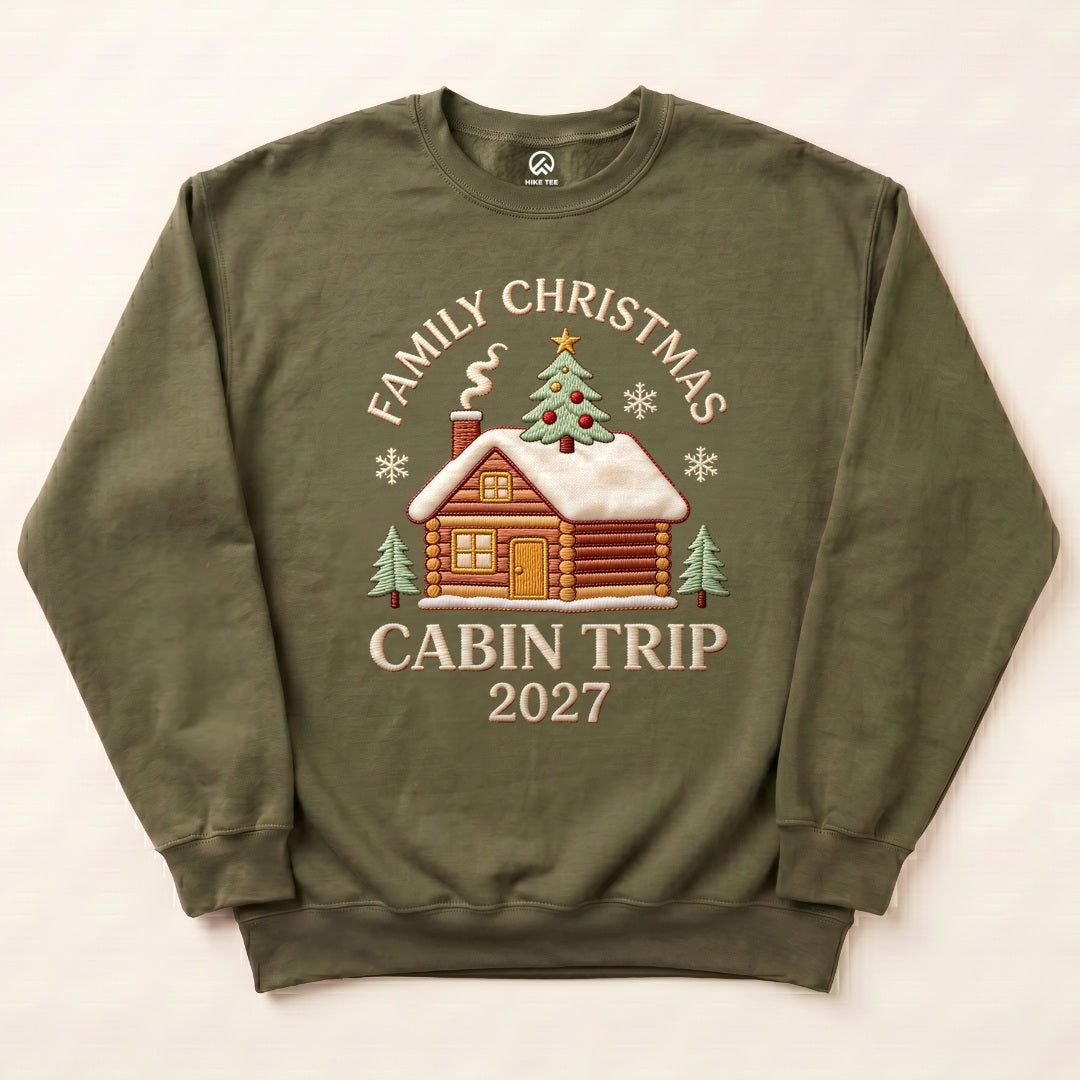 Military Green Family Christmas Cabin Trip 2027 Sweatshirt with a snowy log cabin and Christmas tree graphic