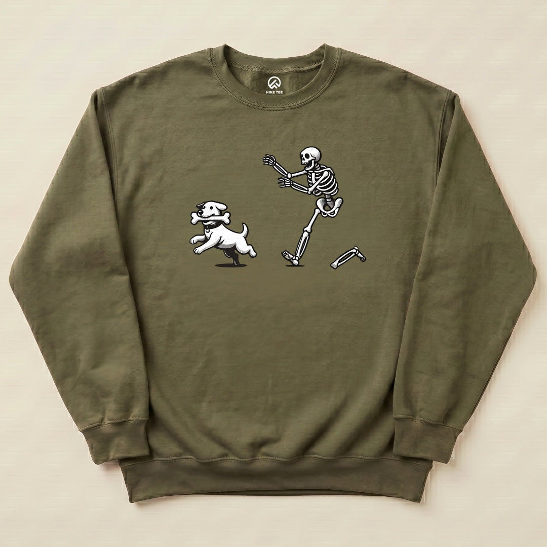 A graphic sweatshirt featuring a playful skeleton chasing a white dog, both set against an olive background.