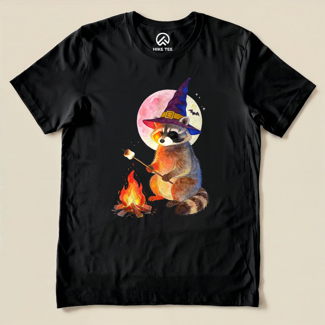 Black Raccoon Witch Campfire Shirt with a raccoon witch roasting a marshmallow by a campfire under a pink moon graphic