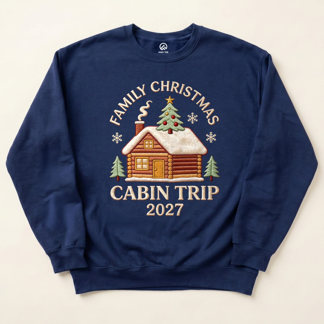 Navy Family Christmas Cabin Trip 2027 Sweatshirt with a snowy log cabin and Christmas tree graphic