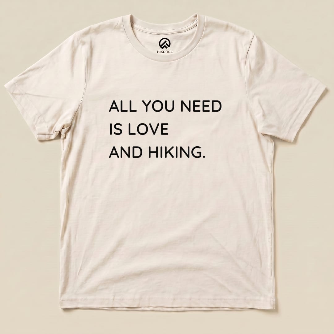 A graphic t-shirt featuring the slogan "ALL YOU NEED IS LOVE AND HIKING" displayed prominently on a light background.