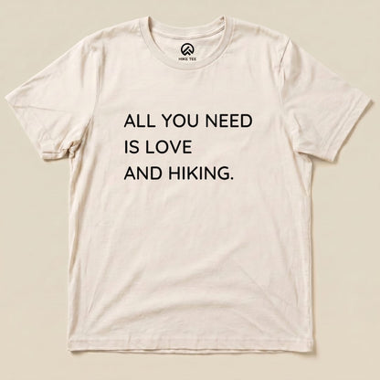 A graphic t-shirt featuring the slogan "ALL YOU NEED IS LOVE AND HIKING" displayed prominently on a light background.