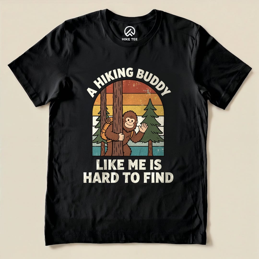 Black graphic t-shirt featuring a playful design of a monkey behind a tree with the text "A Hiking Buddy Like Me Is Hard To Find".