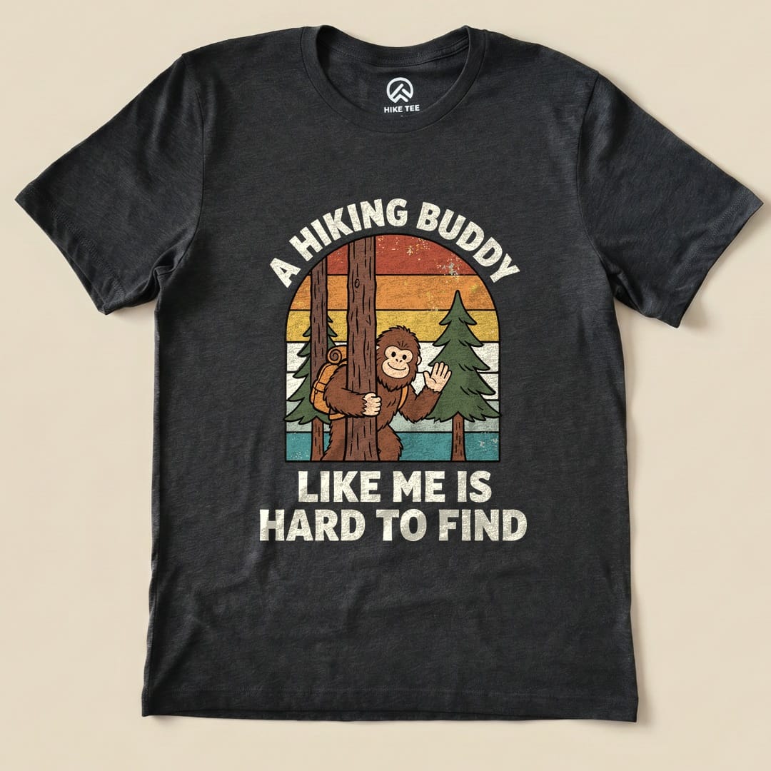 Graphic t-shirt featuring a bigfoot character and trees, with the text "A Hiking Buddy Like Me Is Hard To Find" printed on it.