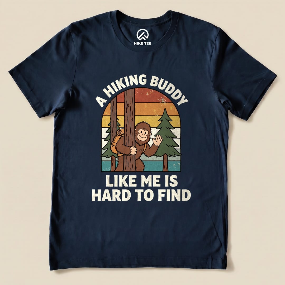 The graphic t-shirt features a playful design of a monkey hiding behind a tree, accompanied by the slogan "A Hiking Buddy Like Me Is Hard To Find.