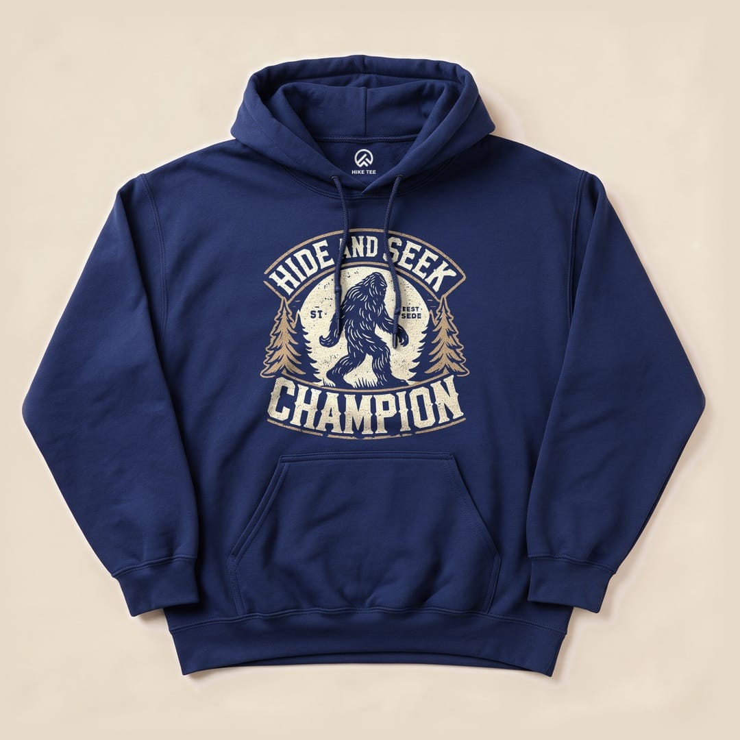 A navy blue hoodie featuring a graphic design of Bigfoot and the text "Hide and Seek Champion" surrounded by pine trees.
