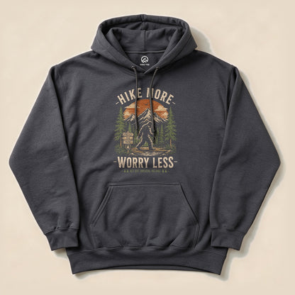 The Hike More, Worry Less Bigfoot Hoodie features a graphic of Bigfoot among trees and mountains, with the slogan above and below.