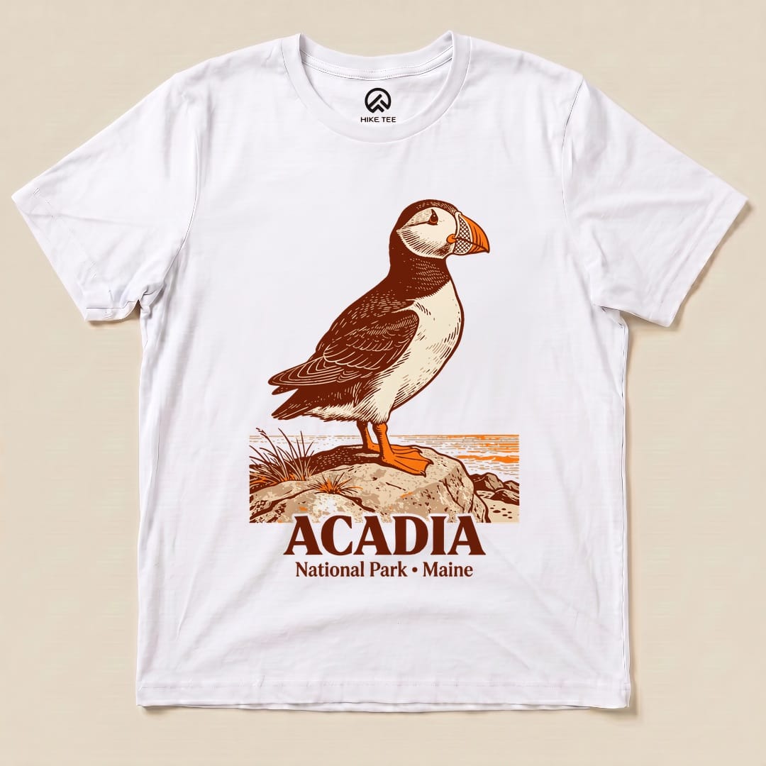 A graphic t-shirt featuring a puffin on a rock with the text "Acadia National Park • Maine" below it.