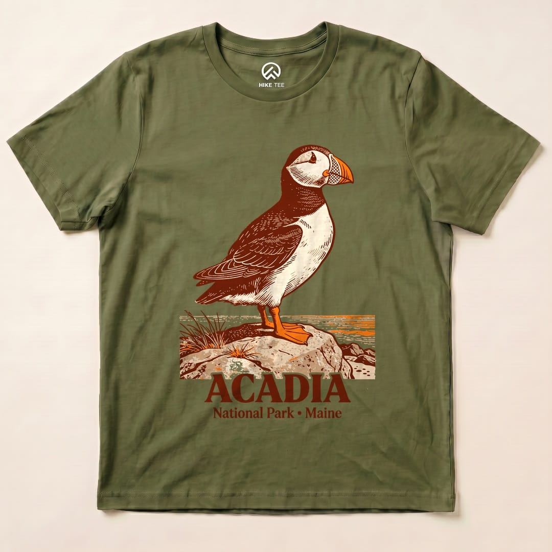 The Acadia National Park Puffin Shirt features a detailed puffin graphic standing on a rock with text below highlighting the park's name.