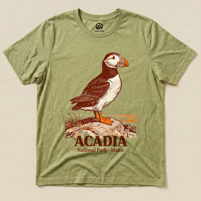The Acadia National Park Puffin Shirt features a detailed illustration of a puffin standing on a rock with the park name below.