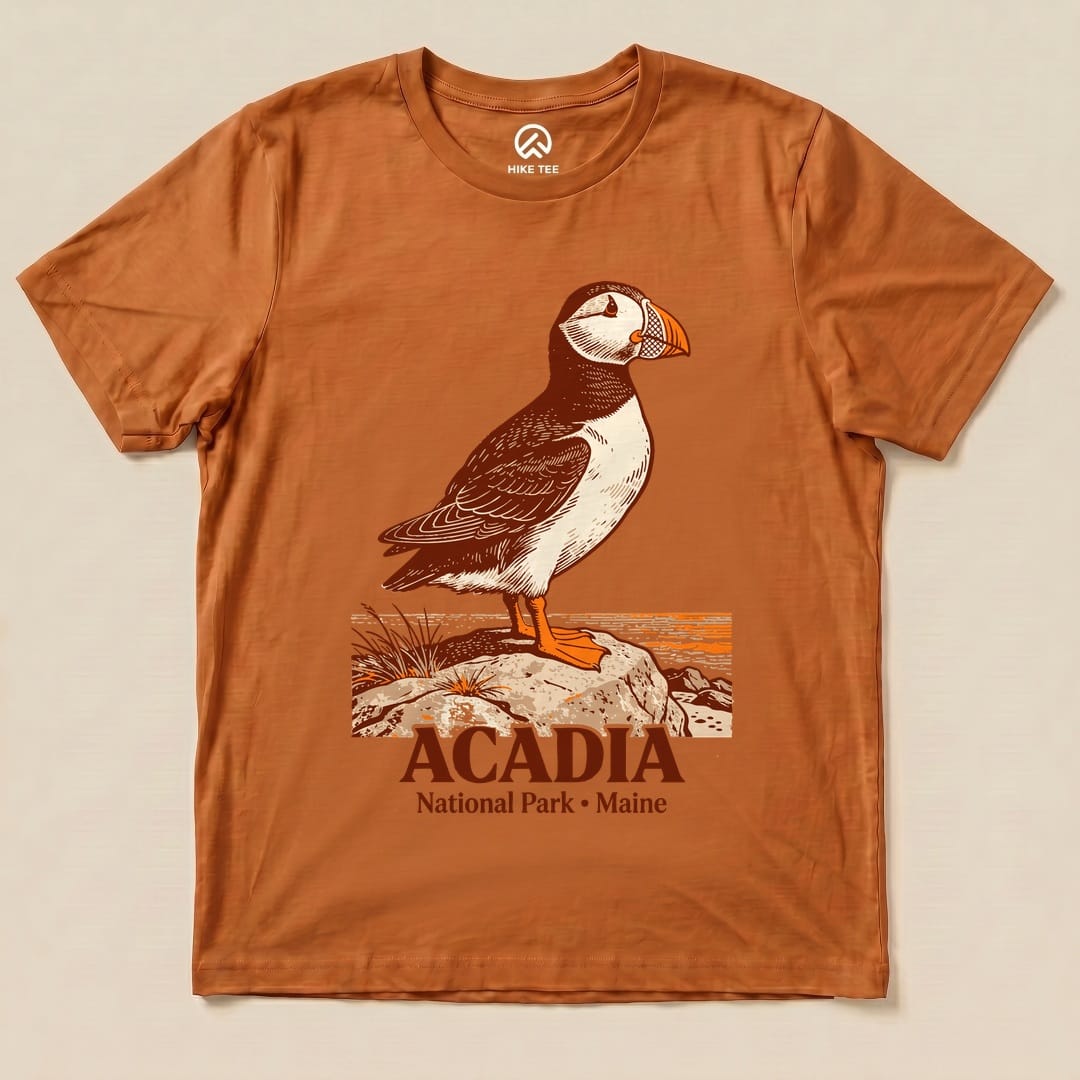 Graphic t-shirt featuring a puffin standing on a rock with the text "Acadia National Park • Maine" below the illustration.