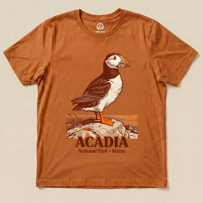 Graphic t-shirt featuring a puffin standing on a rock with the text "Acadia National Park • Maine" below the illustration.