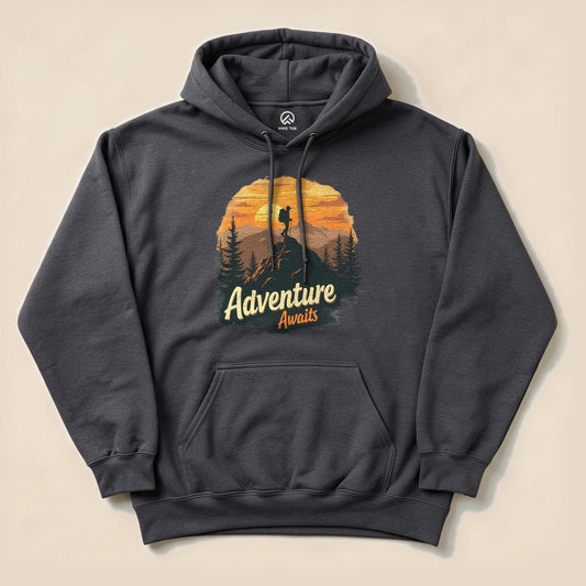 A dark gray hoodie featuring the slogan "Adventure Awaits" with a mountain climber silhouette against a sunset backdrop.