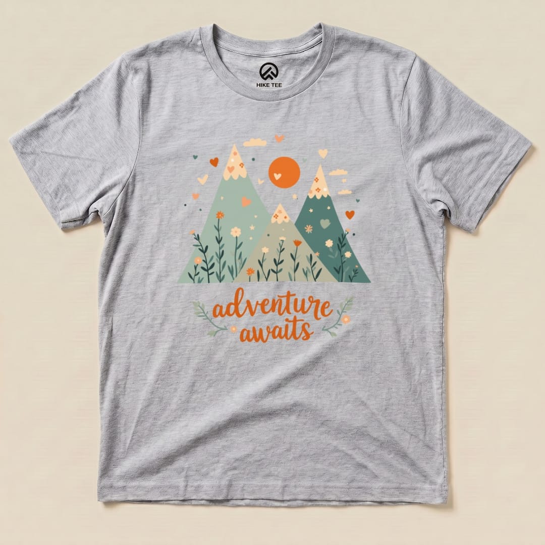 A gray graphic t-shirt displays a colorful mountain scene with the words "adventure awaits" in an inviting font.