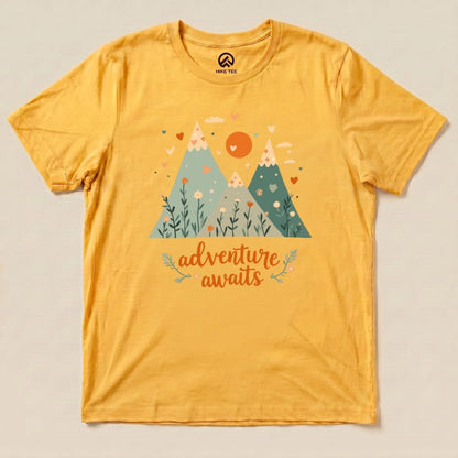 Graphic t-shirt in vibrant yellow featuring a mountain scene with the words "adventure awaits" and decorative flowers.