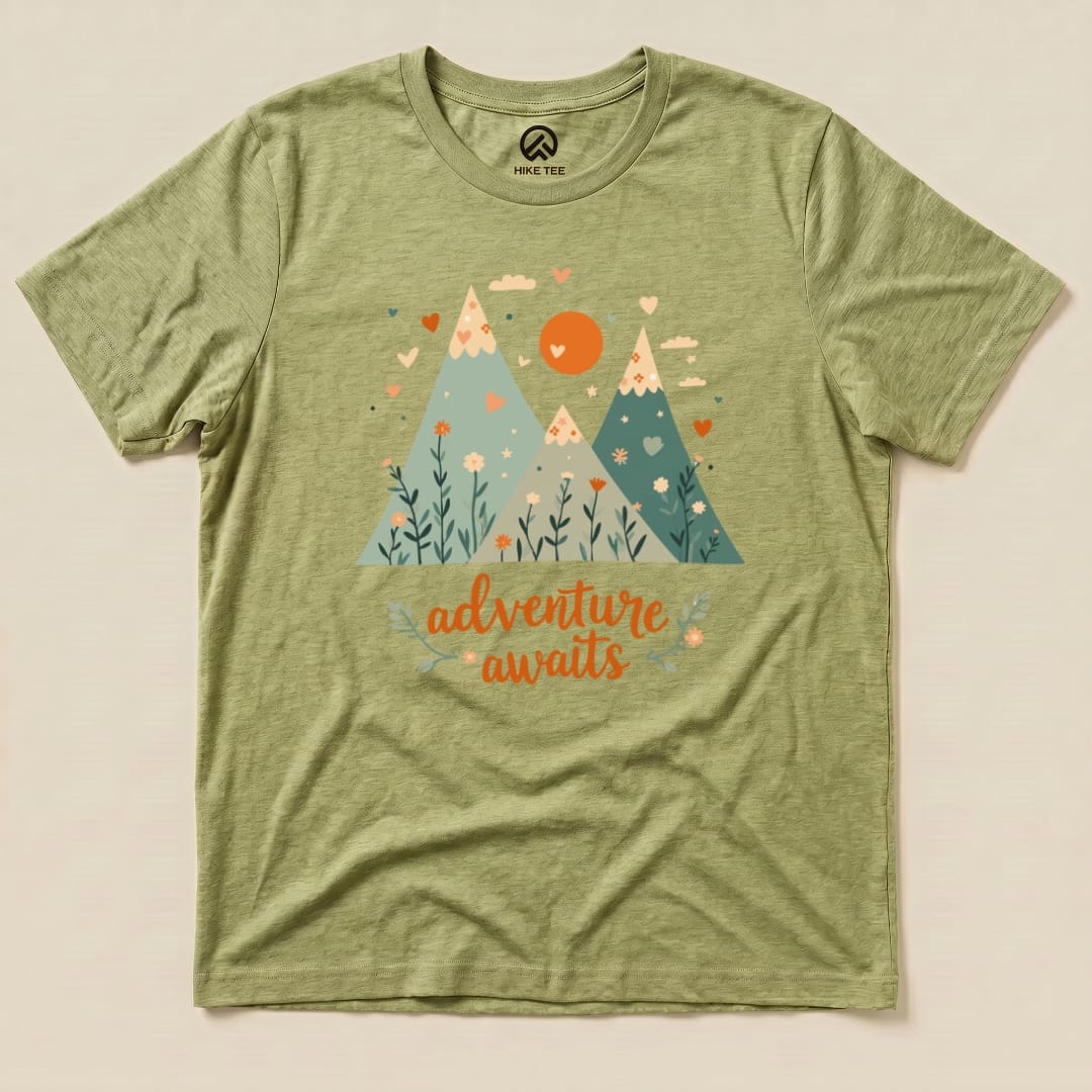 A graphic t-shirt featuring mountains, flowers, and the phrase "adventure awaits" in vibrant colors on an olive green background.