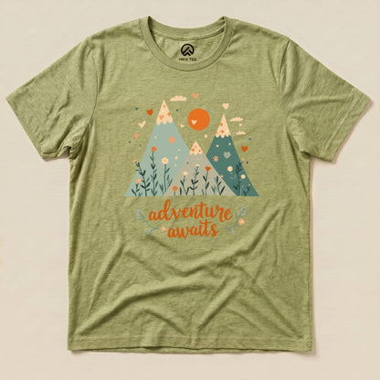 A graphic t-shirt featuring mountains, flowers, and the phrase "adventure awaits" in vibrant colors on an olive green background.