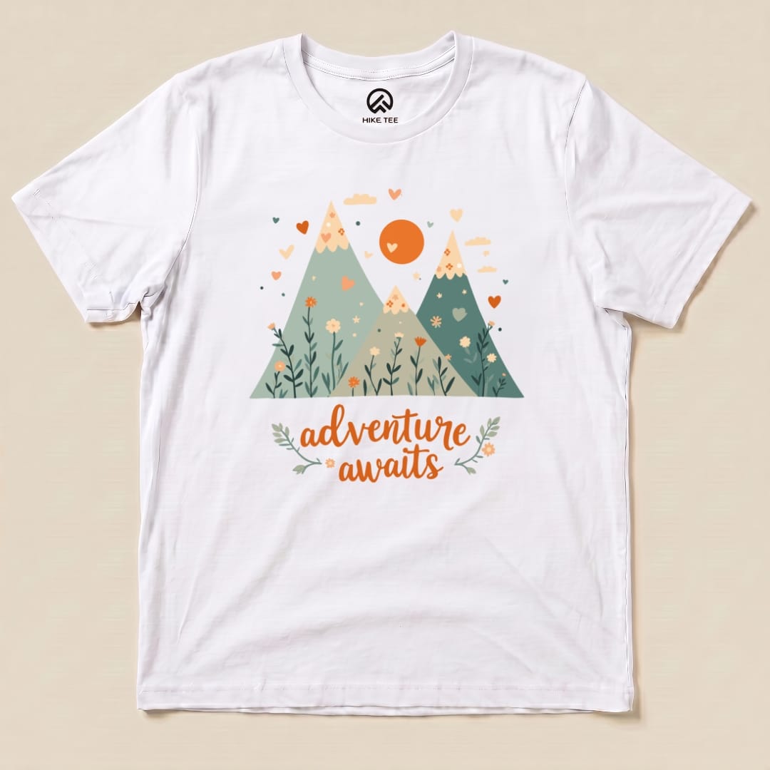 The graphic t-shirt features a colorful design of mountains, flowers, and the phrase "adventure awaits" in playful lettering.