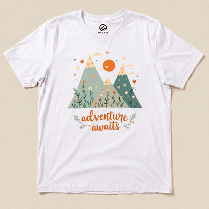 The graphic t-shirt features a colorful design of mountains, flowers, and the phrase "adventure awaits" in playful lettering.