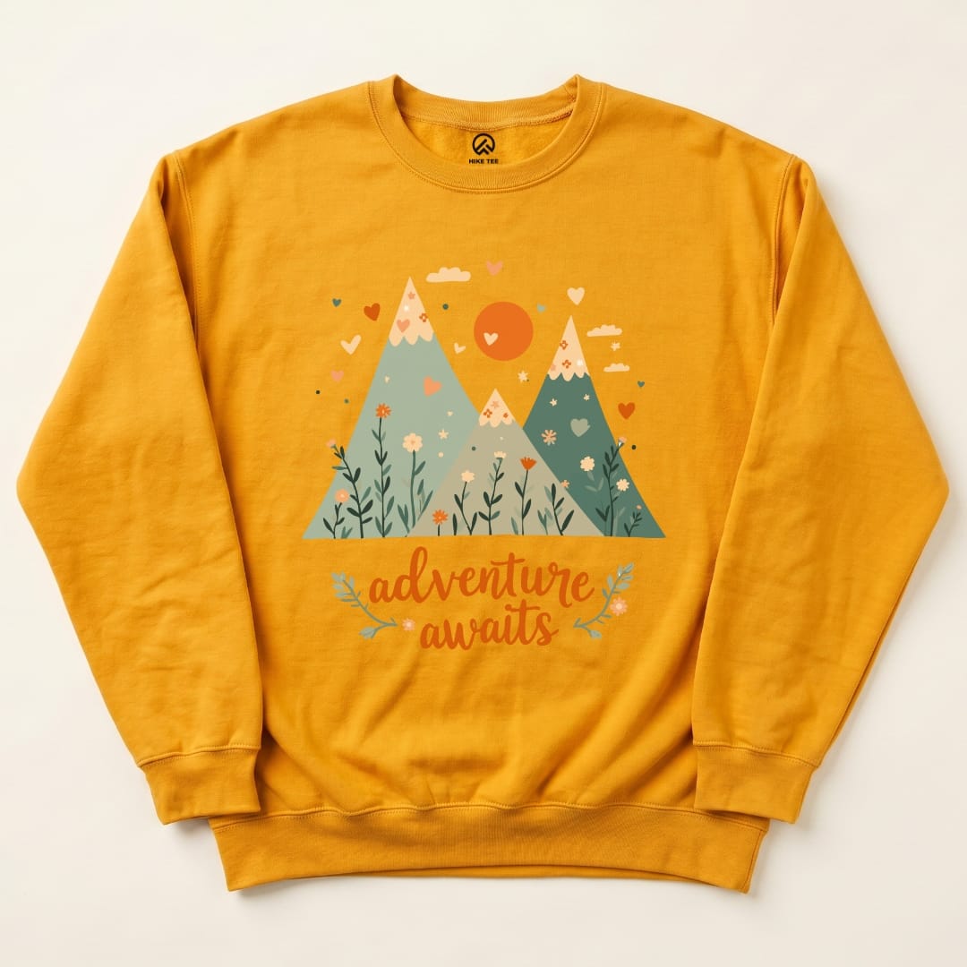 A vibrant yellow sweatshirt featuring a mountain graphic with the slogan "adventure awaits" and colorful floral details.