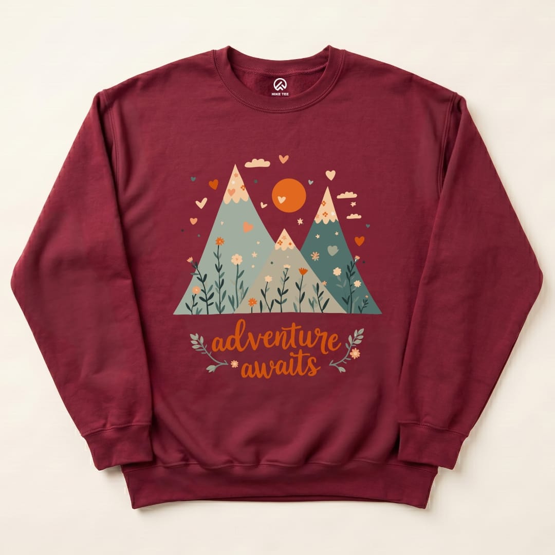 A maroon Adventure Awaits Sweatshirt featuring graphic mountains, a sun, and floral elements with the slogan "adventure awaits.