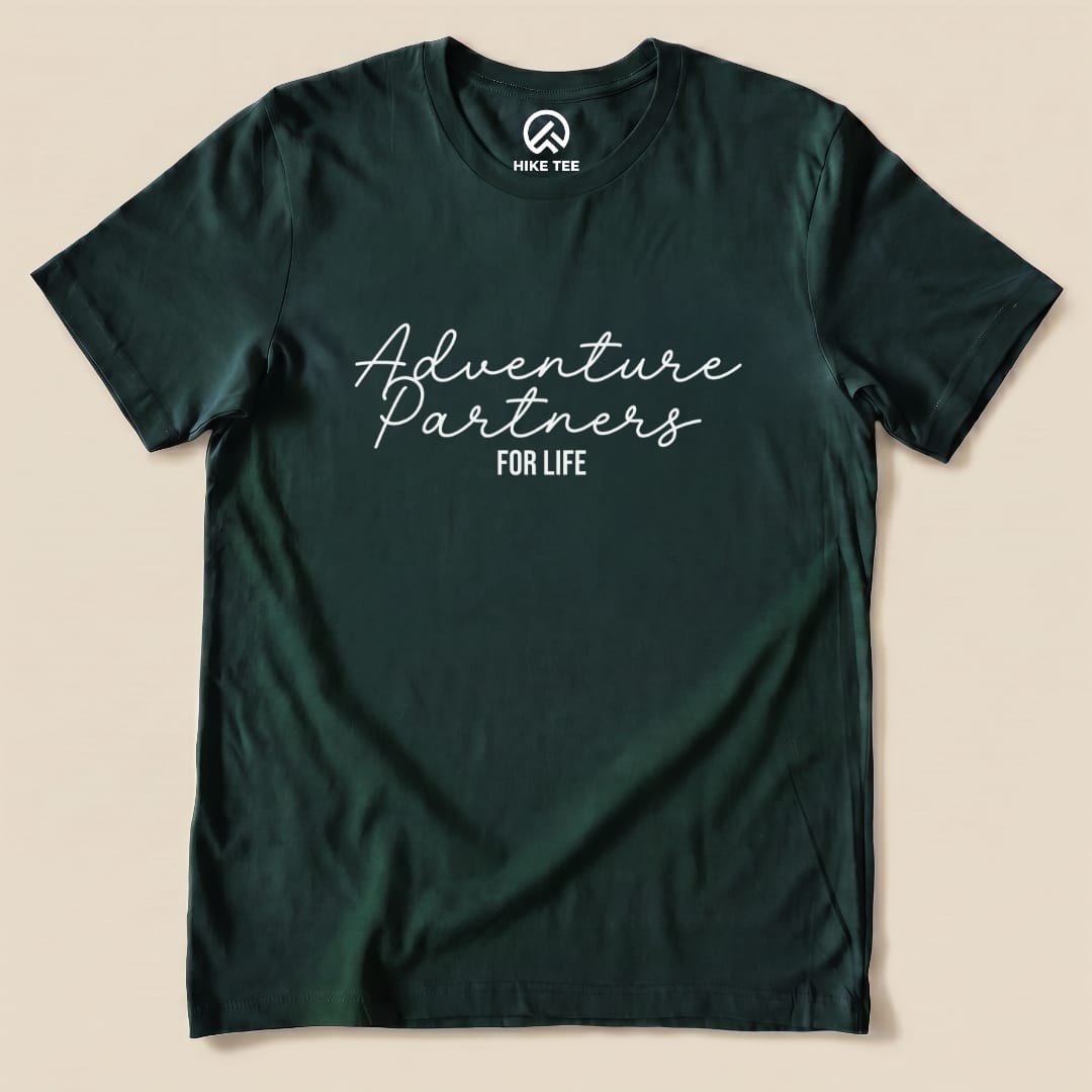 A graphic t-shirt in dark green featuring the slogan "Adventure Partners for Life" in a playful script font.