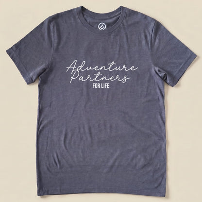 A flat graphic t-shirt in slate gray featuring the text "Adventure Partners For Life" in a stylish, casual font.