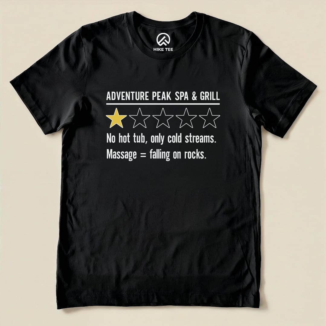 Black graphic t-shirt featuring the slogan "Adventure Peak Spa & Grill" with a one-star rating and humorous text about cold streams.