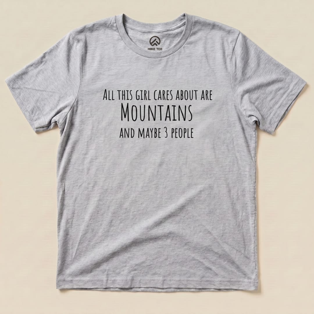 A flat graphic t-shirt labeled "All This Girl Cares Shirt," featuring the text: "All this girl cares about are Mountains and maybe 3 people.