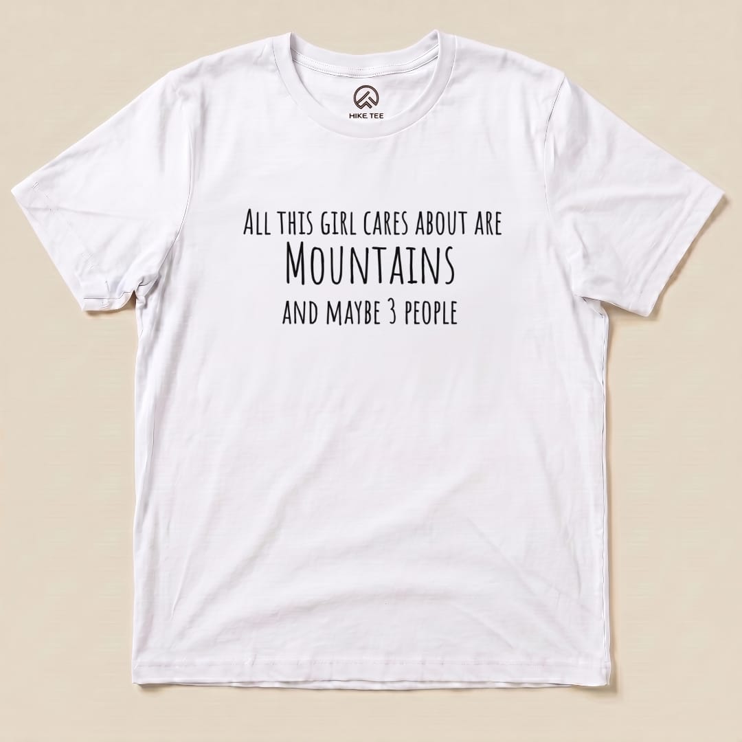 A white graphic t-shirt featuring the text "All This Girl Cares About Are Mountains and Maybe 3 People.