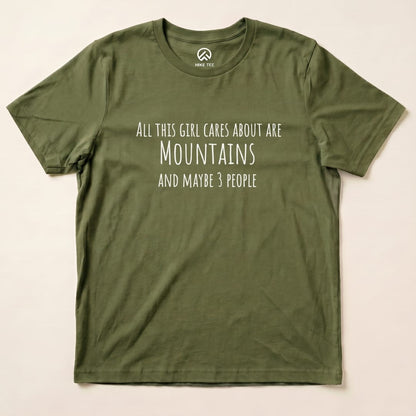 A flat olive green graphic t-shirt features the text "All This Girl Cares About Are Mountains and Maybe 3 People.