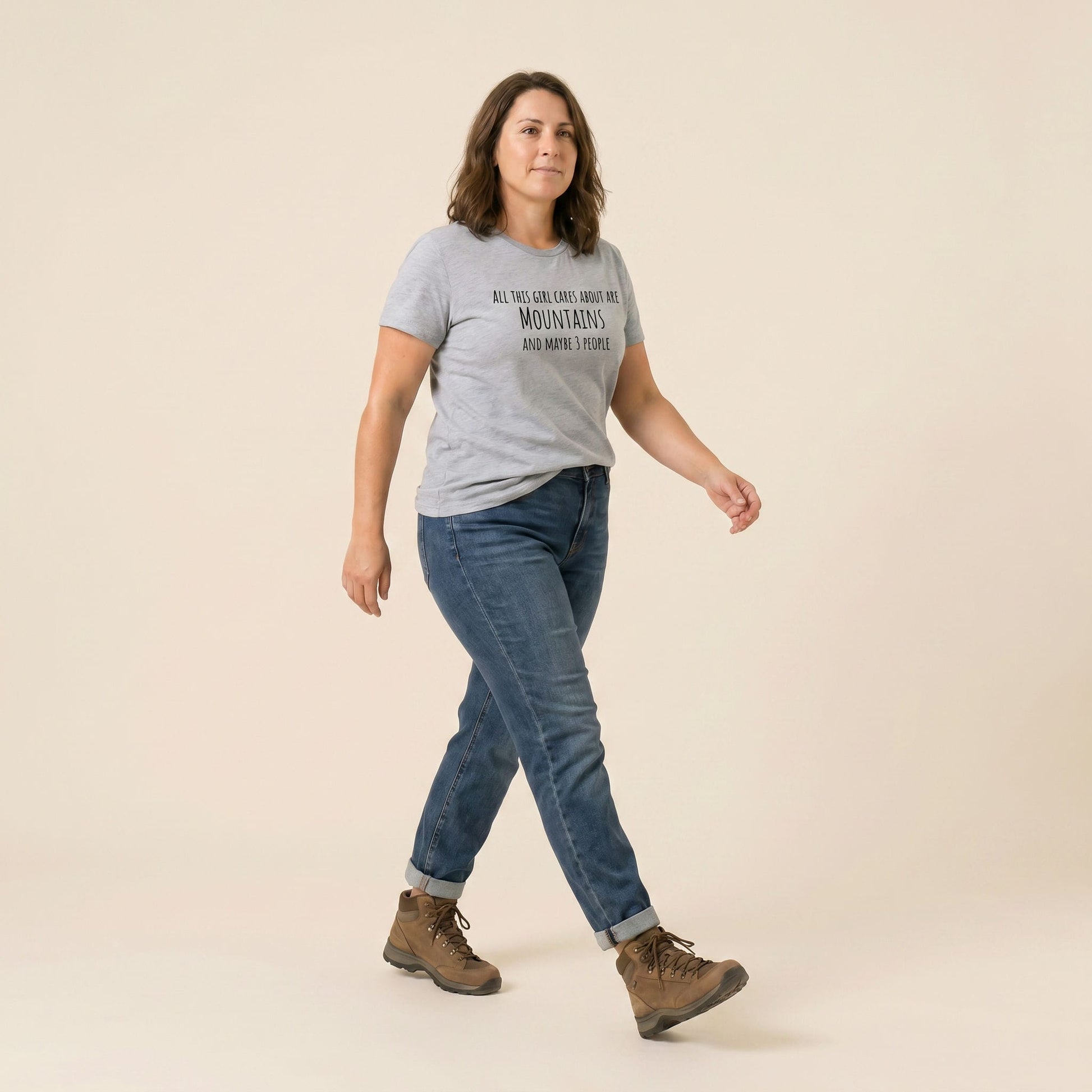 A woman walks confidently in a light gray graphic t-shirt that reads "All This Girl Cares About Are Mountains and Maybe 3 People.