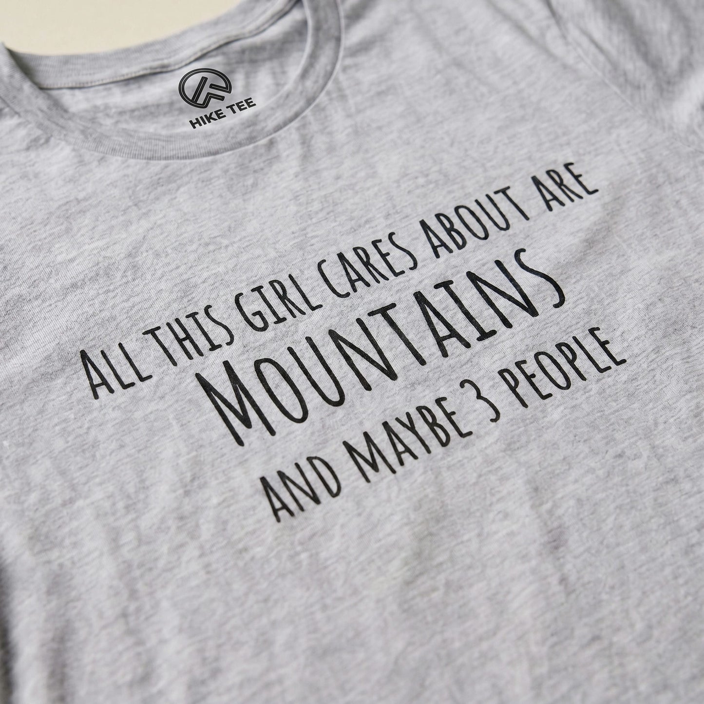 The All This Girl Cares Shirt features bold text stating, "All this girl cares about are MOUNTAINS and maybe 3 PEOPLE" on a gray graphic t-shirt.