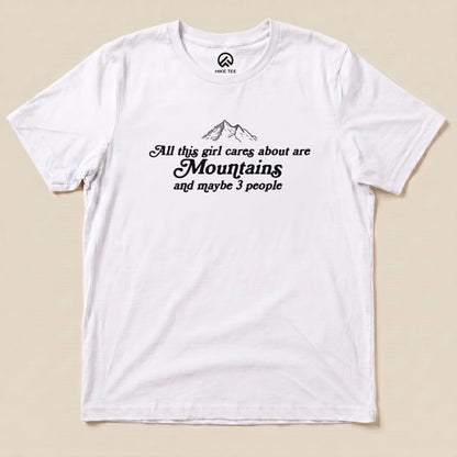 Graphic t-shirt featuring the phrase "All this girl cares about are Mountains and maybe 3 people," set against a white background.