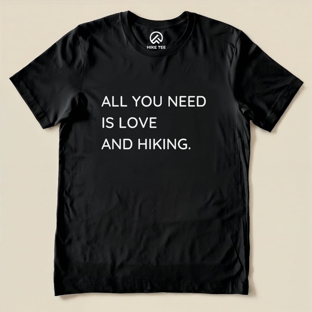 A black graphic t-shirt featuring the phrase "ALL YOU NEED IS LOVE AND HIKING," showcasing a humorous take on outdoor adventures.