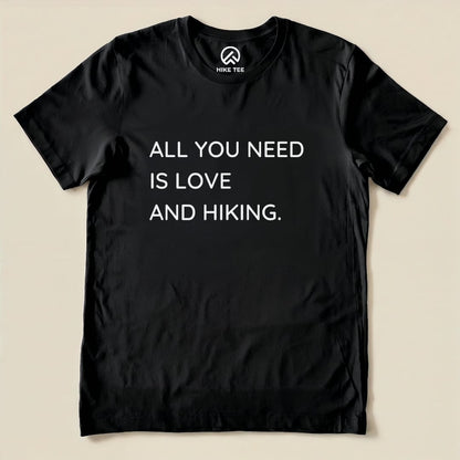 A black graphic t-shirt featuring the phrase "ALL YOU NEED IS LOVE AND HIKING," showcasing a humorous take on outdoor adventures.