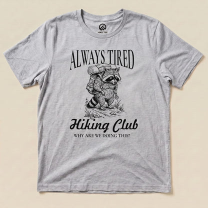 The Always Tired Club Shirt features a raccoon with a backpack and the phrase "Why are we doing this?" in a humorous graphic design.