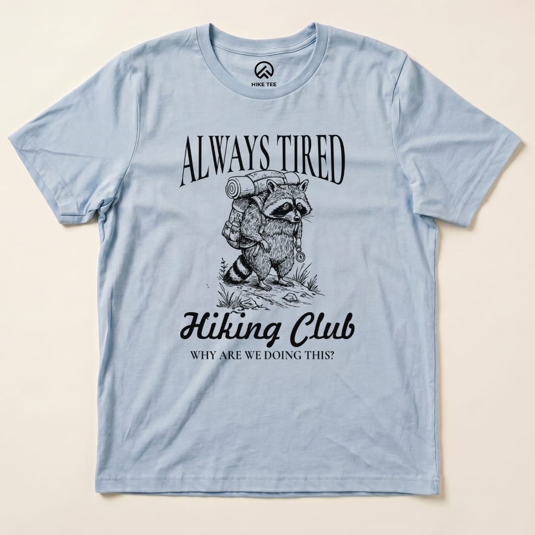 The Always Tired Club Shirt features a raccoon carrying a backpack, with the text "Always Tired Hiking Club" and "Why are we doing this?" printed below.